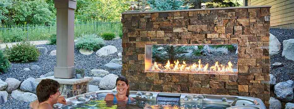 Ready-to-finish Outdoor Gas Fireplace by THe Outdoor GreatRoom Company lifestyle with a hottub in the foreground with people in it